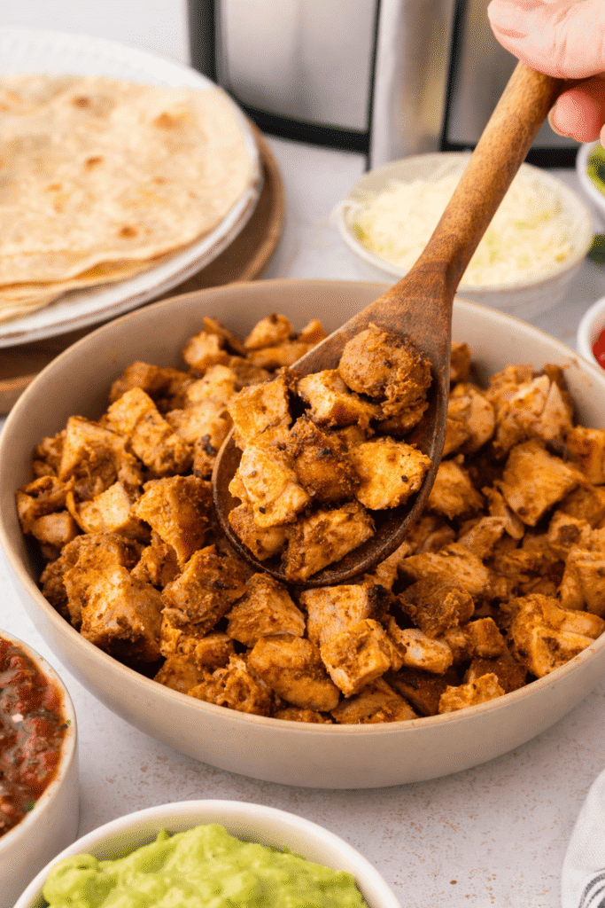 Goldbraun gebratenes Hähnchen in Würfeln auf einem Holzlöffel über einer Schüssel, saftig gewürzt und frisch zubereitet.