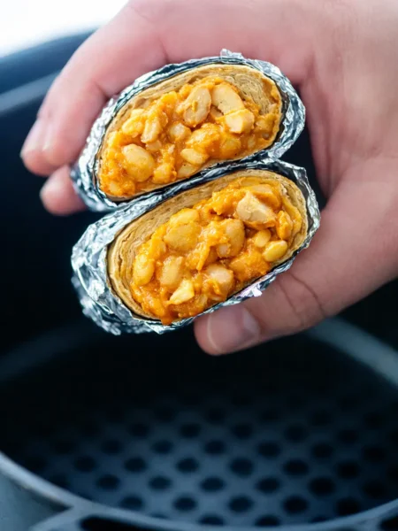 Burrito im Airfryer halbiert mit cremiger Füllung aus Hähnchen und Sauce in der Hand gehalten