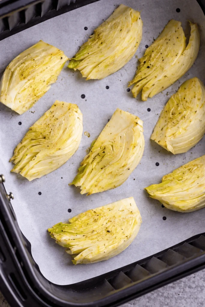 Gewürzte Fenchelspalten im Heißluftfritteuse-Korb auf Backpapier vor dem Garen
