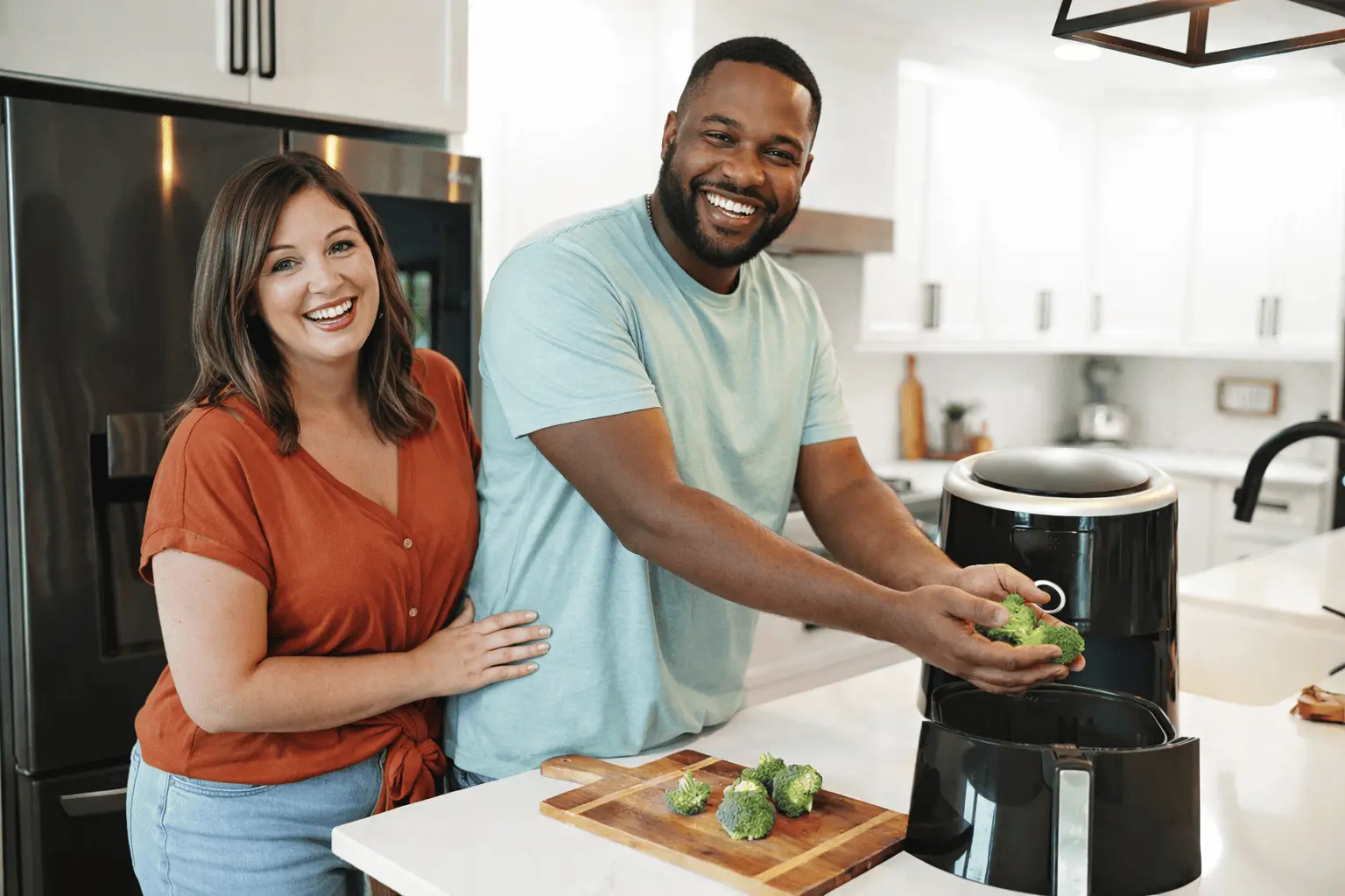 Ein glückliches Paar kocht zusammen in einer modernen Küche und bereitet Brokkoli mit einem Airfryer zu. Airfryer Rezepte machen das Kochen einfach und schnell.