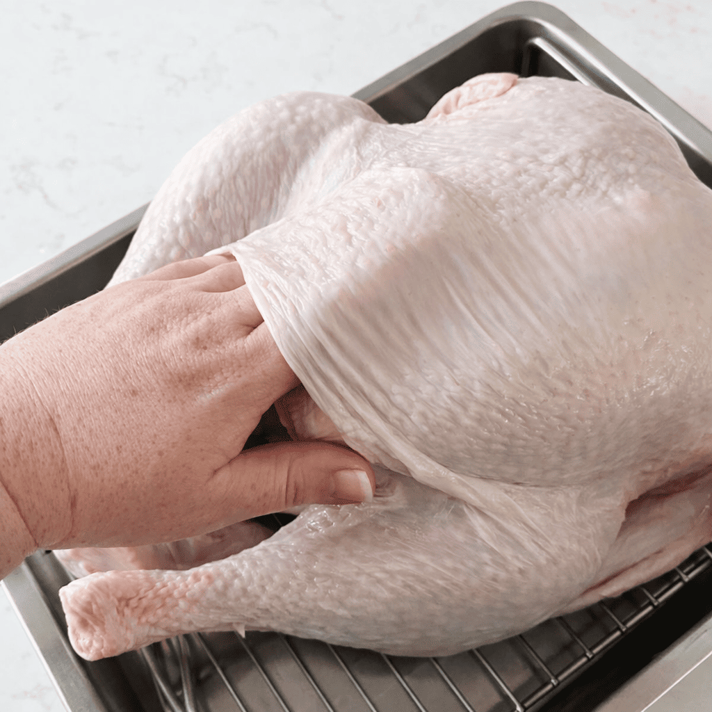 Hand schiebt Kräuterbutter unter die Haut eines rohen Truthahns vor der Zubereitung im AirFryer