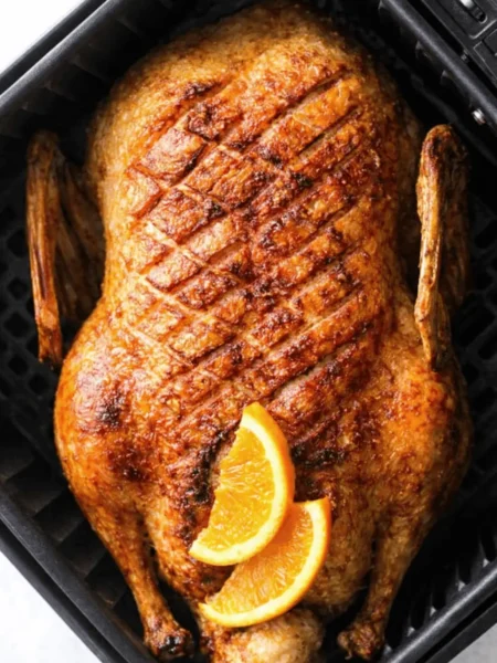 Knusprige, goldbraune Airfryer Ente in einem schwarzen Korb, garniert mit frischen Orangenscheiben.