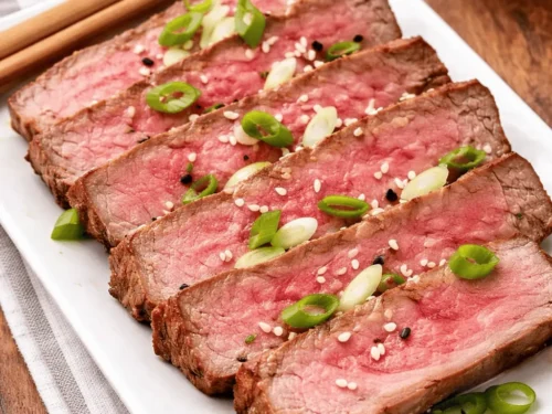 Saftig gebratenes Airfryer Thunfischsteak in Scheiben geschnitten mit Sesam und Frühlingszwiebeln auf weißem Teller