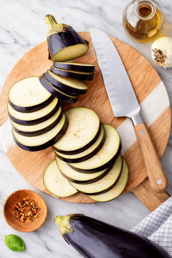 Geschnittene Auberginen in Scheiben auf einem Holzbrett mit Messer für Auberginen Airfryer Rezept.