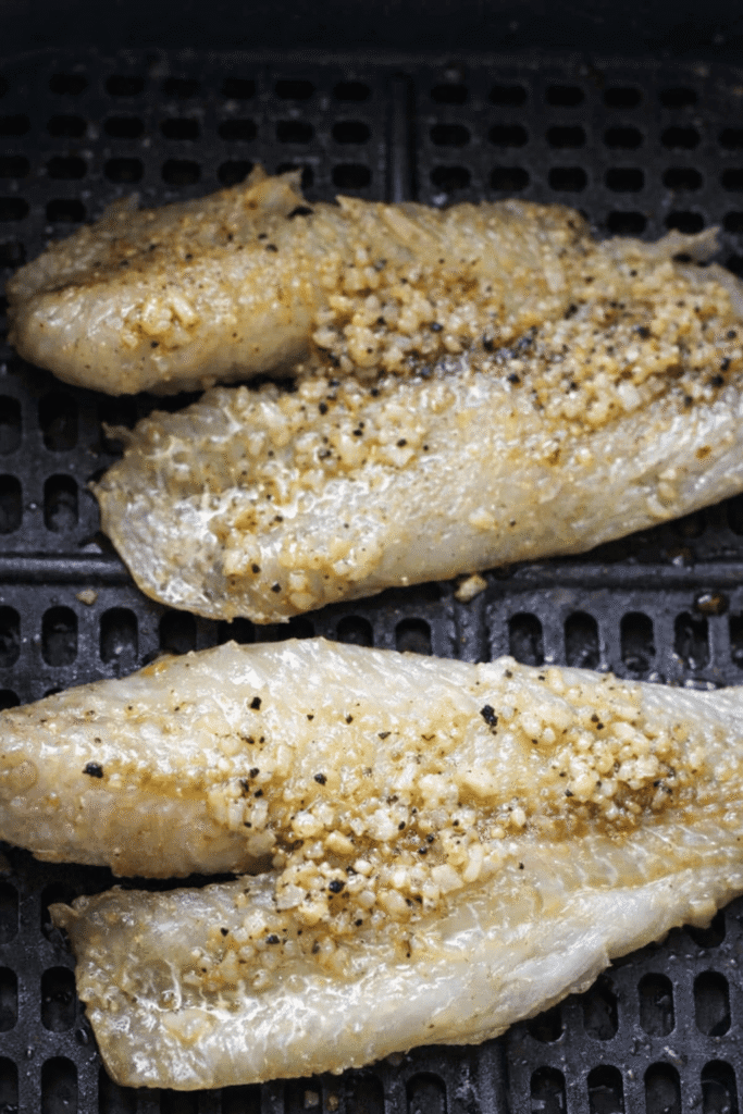 Zwei gegarte Seelachsfilets mit Knoblauch-Butter im Korb der Heißluftfritteuse.