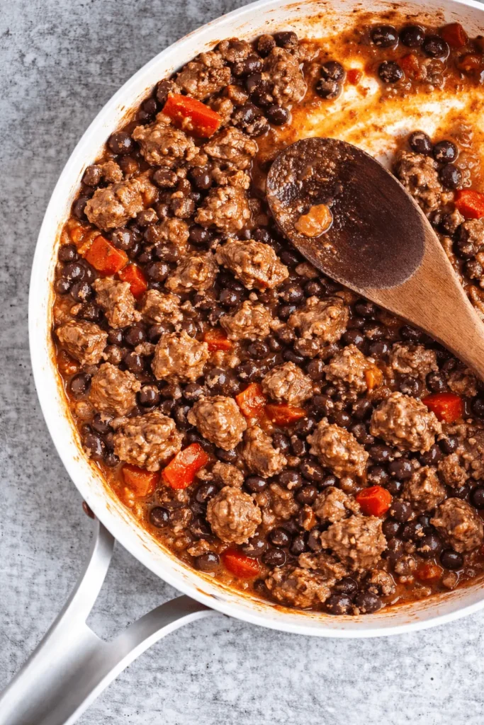 Hackfleisch mit schwarzen Bohnen und Tomaten in einer Pfanne beim Anbraten für Airfryer gefüllte Paprika.