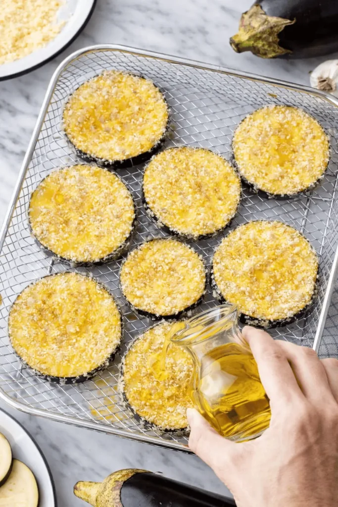Olivenöl wird über panierte Auberginenscheiben für Aubergine Airfryer gegossen