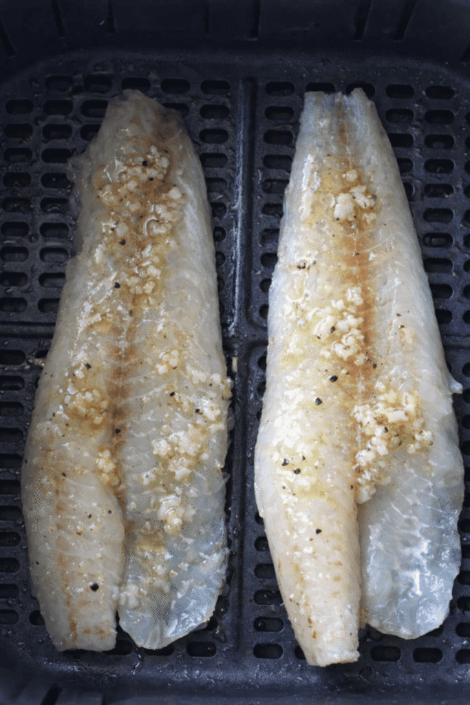 Zwei rohe Seelachsfilets mit Knoblauch-Butter in einem Airfryer-Korb.