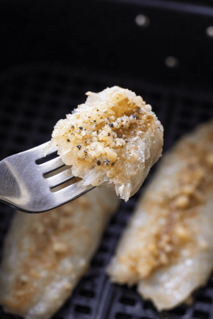 Gabel mit einem zarten Stück Seelachs mit Knoblauch-Butter aus der Heißluftfritteuse.