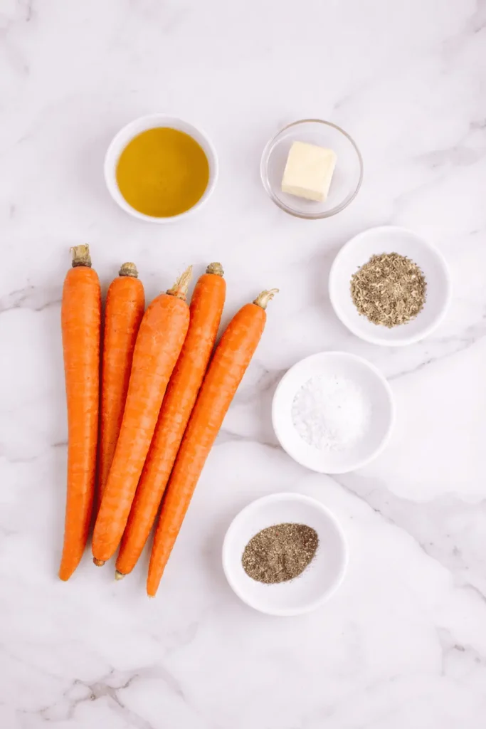 Frische Karotten mit Olivenöl, Butter, Kräutern, Salz und Pfeffer auf einer weißen Marmoroberfläche, bereit zum Rösten.